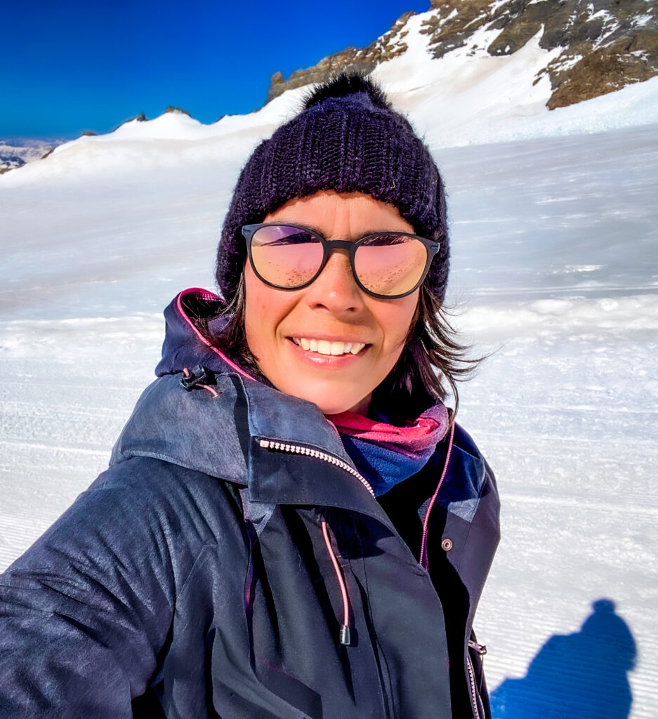 Amandine Devergies en selfie au Jungfraujoch, bonnet noir et veste de ski, avec le plateau glaciaire alpin en arrière-plan.
