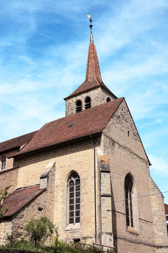 Église en pierre de taille avec clocher pointu et tuiles brunes, ciel bleu, Moudon, Vaud, Suisse