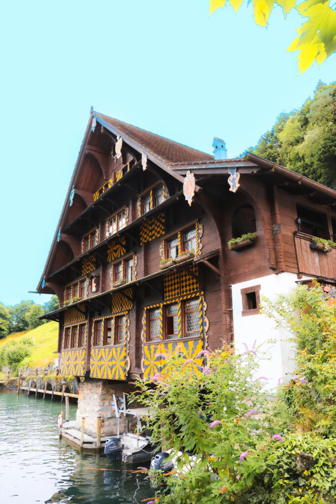 Chalet suisse en bois aux motifs géométriques jaune et noir au bord d'un lac, ponton et bateaux, végétation estivale luxuriante