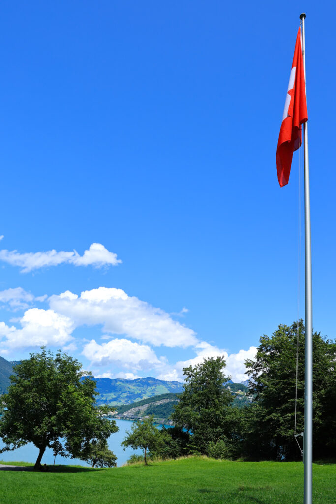 Drapeau suisse sur un mât au Grütli, avec la prairie et le lac des Quatre-Cantons en arrière-plan sous un ciel d'été.