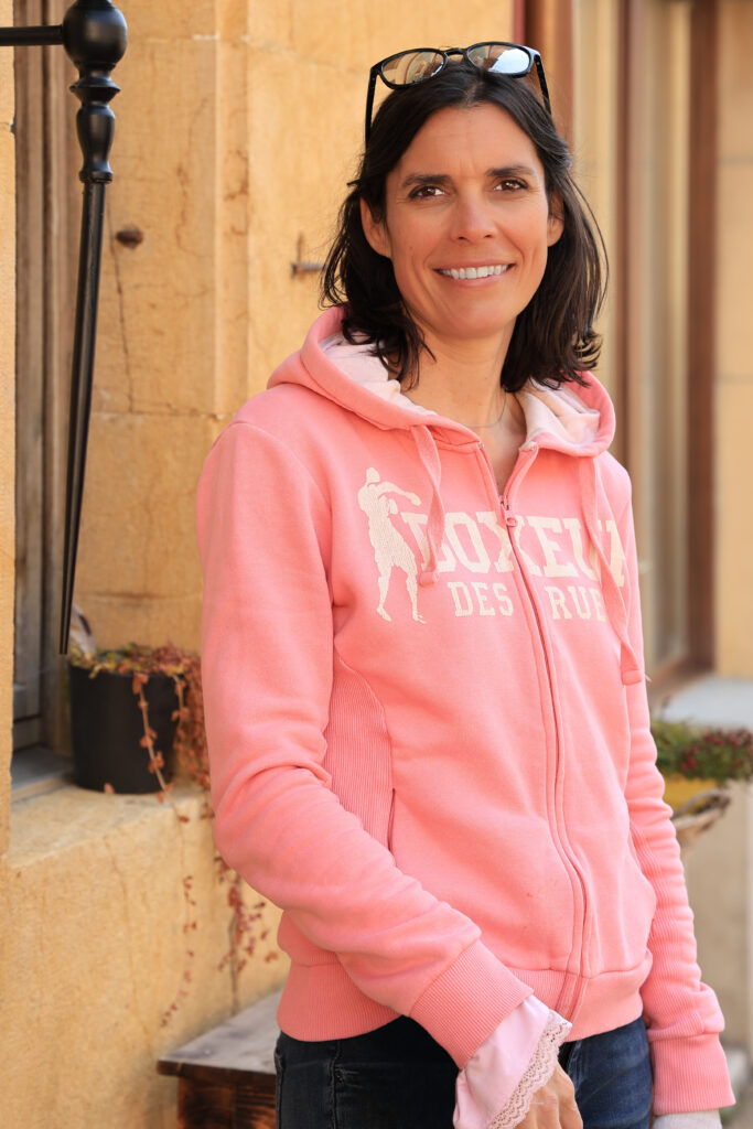 Portrait d'Amandine Devergies souriante devant les murs en pierre jaune du Landeron, Neuchâtel.
