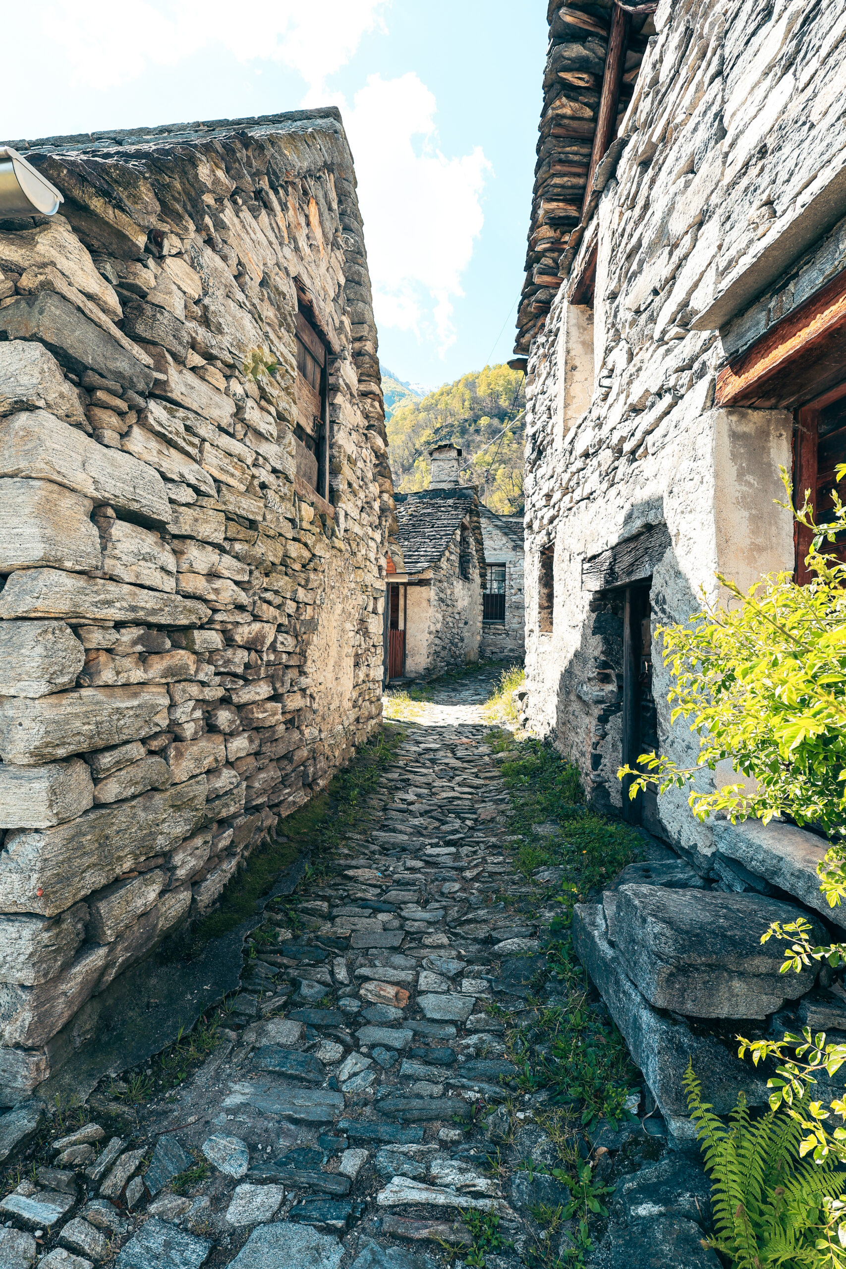 Ruelle pavée d'un village en pierre du Tessin, maisons anciennes et ciel bleu entre les toits