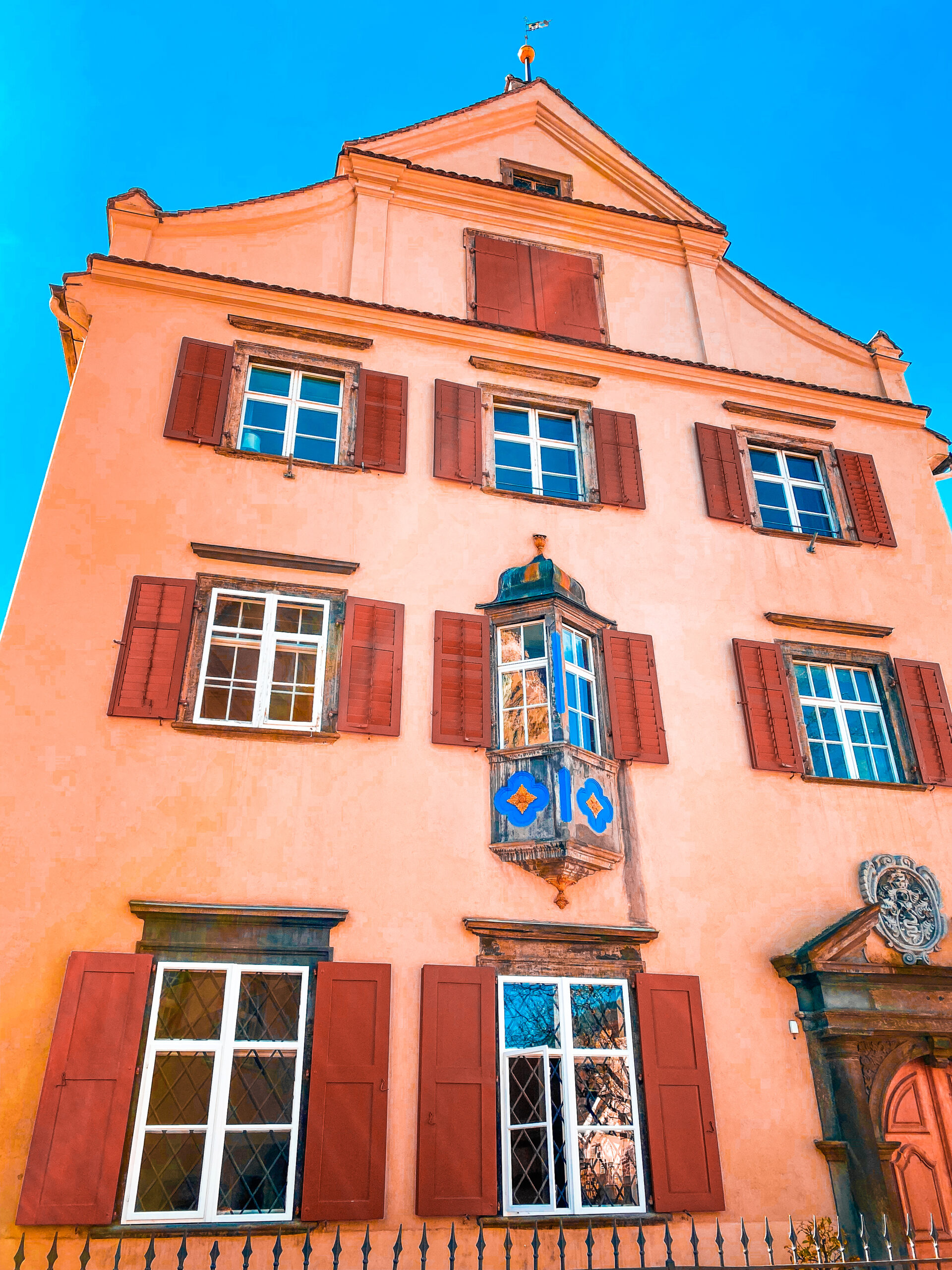 Façade saumon aux volets bordeaux et oriel baroque, vieille ville de Coire, Grisons, ciel bleu