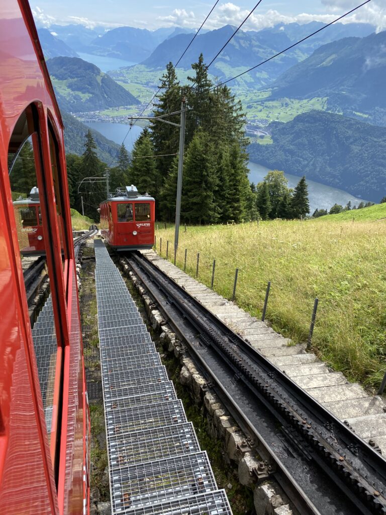 Train à crémaillère rouge grimpant une montagne suisse, vue sur la vallée et un lac